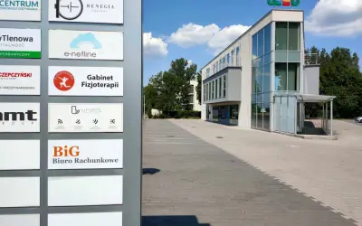 Tablica z nazwami firm, w tym "BiG Biuro Rachunkowe", przed nowoczesnym budynkiem biurowym.