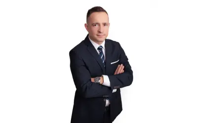Mężczyzna w garniturze ze skrzyżowanymi rękami, na białym tle.
