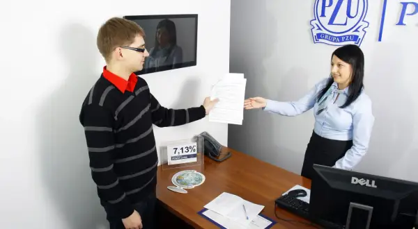 Mężczyzna podaje dokumenty kobiecie przy biurku w biurze PZU.