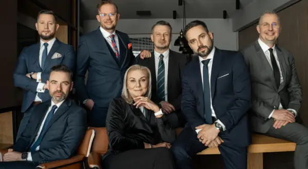 Grupa siedmiu profesjonalistów w garniturach, pozujących do zdjęcia w biurze.