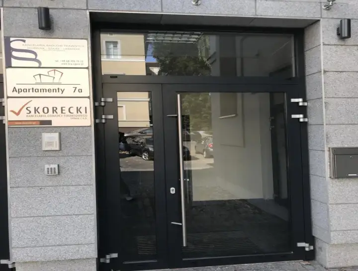 Drzwi wejściowe do budynku z tabliczkami: "Apartamenty 7a" i "SKORECKI Kancelaria Doradcy Finansowego".